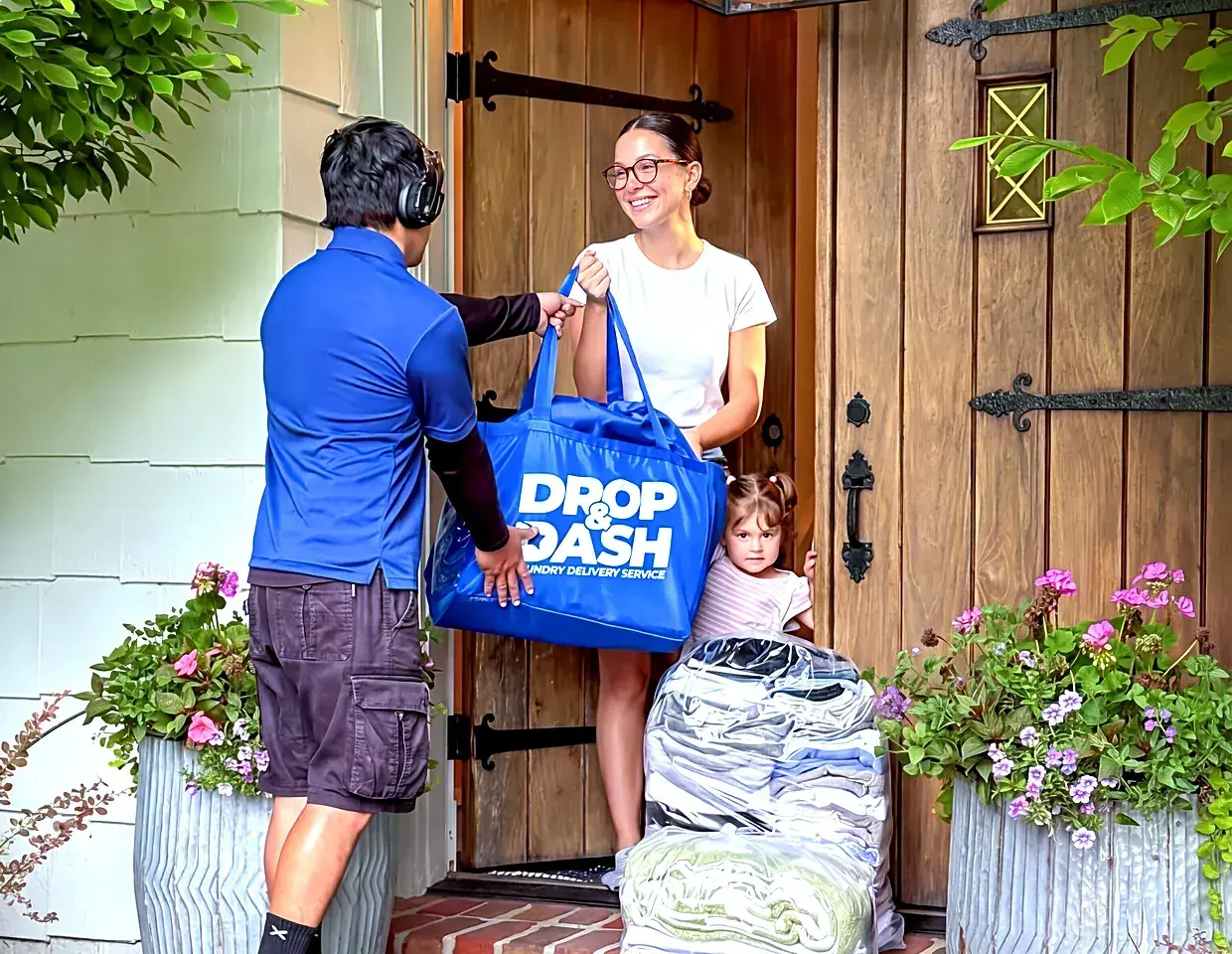 A Drop & Dash driver handing a blue bag of clean, folded laundry to a smiling customer at her front door